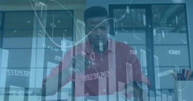 Animation of financial graphs and data over african american man in office. Business, finance, economy, data processing and technology concept digitally generated video.