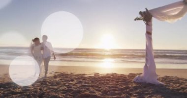 Animation of dots over happy african american newly married couple on beach. Holidays, vacations love, marriage concept digitally generated video.