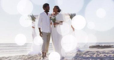 Animation of dots over happy african american newly married couple on beach. Holidays, vacations love, marriage concept digitally generated video.