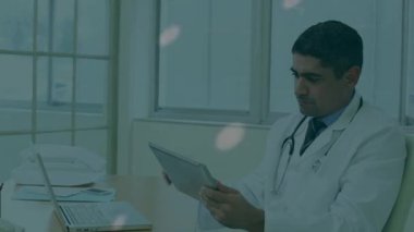 Animation of spinning globe over biracial senior male doctor using digital tablet at hospital. Medical healthcare and technology concept