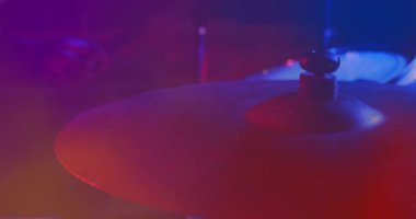 Video of hands of drummer playing drum kit, cymbal in foreground, red and blue light. Live music, creativity, performance and entertainment concept.