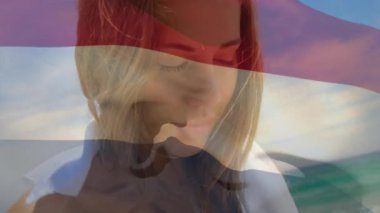 Animation of flag of netherlands over caucasian woman at beach. National flags, patriotism and holiday concept digitally generated video.
