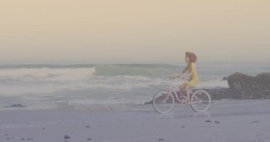 Spots of light against african american woman riding a bicycle at the beach. pedal day awareness concept