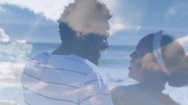 Sahildeki Afro-Amerikan çifti üzerindeki bulutların animasyonu. Tatil ve dijital arayüz kavramı dijital olarak oluşturulmuş video.