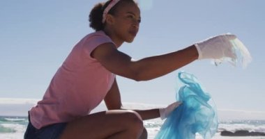 Animation of save the ocean text with icons over african american woman cleaning at beach. Global ecology and digital interface concept digitally generated video.