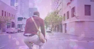 Spots of light against rear view of african american man riding a bicycle on the street. pedal day awareness concept
