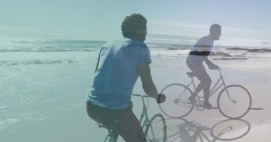 Afrika kökenli Amerikalı bir adamın Afrika kökenli bir Amerikalının plajda bisiklet sürüşünü canlandırıyor. Tatil ve dijital arayüz kavramı dijital olarak oluşturulmuş video.