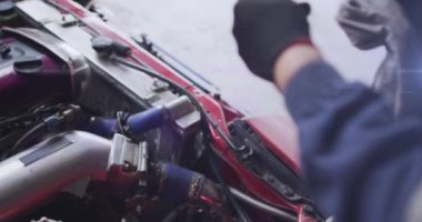 Animation of blue light moving over hands of asian mechanic cleaning vehicle part with fabric. Garage, digital composite, automobile, repairing, breakdown and service occupation concept.