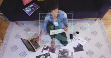 Animation of profiles icons against biracial woman reading documents and using laptop. Social media networking and business technology concept
