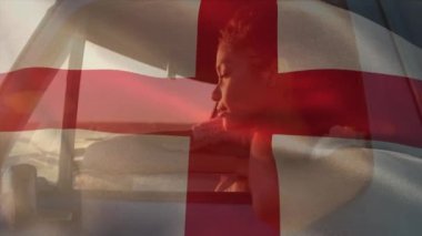 Animation of waving england flag over african american woman enjoying breeze through car window. Digital composite, multiple exposure, leisure, travel, vacation, patriotism and identity concept.