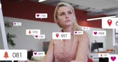 Animation of social media notifications processing data over caucasian woman working at office desk. Global communication network, digital interface and social media concept digitally generated video.