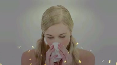 Animation of golden confetti falling over caucasian sick woman with tissue blowing her nose. Covid-19 pandemic concept