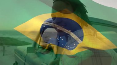 Animation of brazilian flag waving over portrait of african american man standing by pick-up truck. Dreadlocks, happy, digital composite, multiple exposure, beach, vacation, patriotism, and identity.