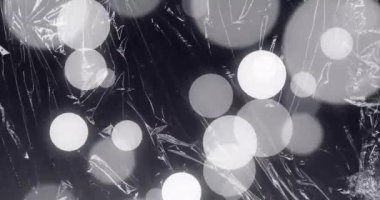 Animation of grey and white spots of light over light on moving shiny black plastic. Creativity, imagination and change, monochrome abstract background concept digitally generated video.