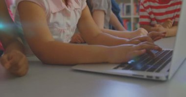 Animation of glowing light over diverse school children using laptop in classroom. Education, learning and development concept digitally generated video.