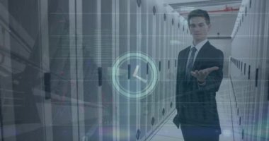 Animation of clock icon over caucasian businessman holding an invisible object at server room. Global economy and business data storage technology concept