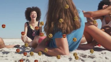 Animation of smiling and love emojis over diverse group of happy friends relaxing on sunny beach. Global communication network, holidays and social media concept digitally generated video.