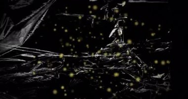 Animation of yellow particles floating over light on moving shiny black plastic. Nature, science and technology, abstract background concept digitally generated video.