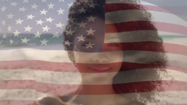 Animation of flag of america over portrait of smiling african american young woman at beach. Digital composite, multiple exposure, curly hair, vacation, nature, patriotism and identity concept.