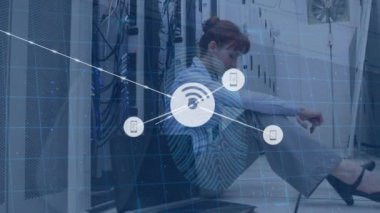 Animation of network of communication icons and fingerprint scan over woman sitting in server room. Global communication, business network and data security concept digitally generated video.