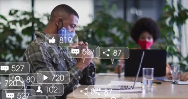 Sosyal medya simgelerinin animasyonu ve dizüstü bilgisayar kullanarak yüz maskesi takan melez bir adam üzerinde numaralar. Dijital olarak oluşturulan küresel sosyal medya, bağlantılar ve covid 19 pandemik konsept.