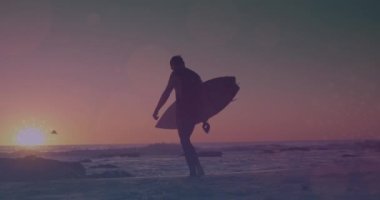 Deniz kenarında sörf tahtasıyla yürüyen adamın üzerinde parlayan ışıkların animasyonu. Egzersiz, refah, spor, açık hava yaşam tarzı, yaz ve tatil konsepti dijital olarak oluşturulmuş video.