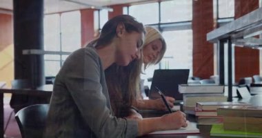Animation of trading board and graphs over caucasian teachers writing in books on desk at school. Digital composite, multiple exposure, data, investment, office, education, technology concept.