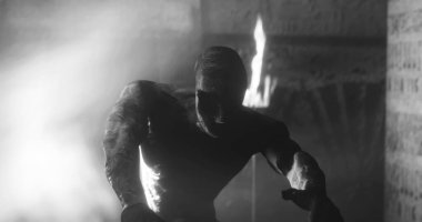 Image of scary zombie mummy walking in dark crypt with burning torches, in black and white. Halloween fear, horror and suspense concept digitally generated image.