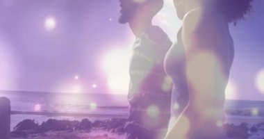 Animation of light spots over biracial couple at beach. Holidays and digital interface concept digitally generated video.