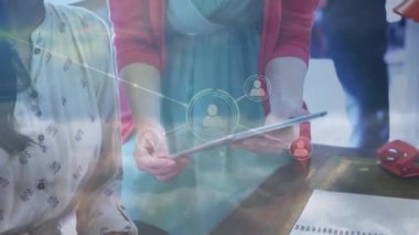 Animation of network of profile icons over two diverse women discussing over a digital tablet. Global networking and business technology concept