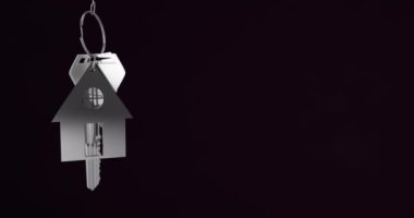 Animation of silver house keys hanging against black background with copy space. Relocation and real estate concept