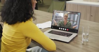 Video of biracial woman having video call on laptop. Business, communication and working in office with technology concept.