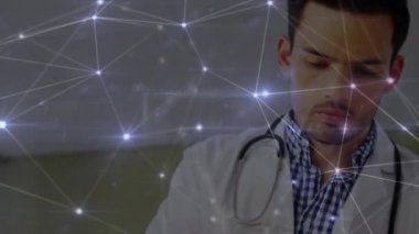 Animation of glowing network of connections over caucasian male doctor reading reports at hospital. Medical healthcare and technology concept