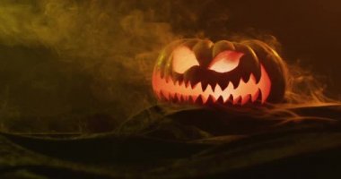 Video of halloween carved pumpkin with smoke and orange light on black background. Halloween, autumn, tradition and celebration concept.
