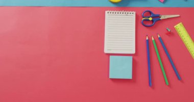 Video of notebook with copy space and school items on pink and blue background. School equipment, tools, learning and education concept.