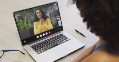 African american woman using laptop for video call, with business colleague on screen. Business communication technology and remote home working, digital composite video.