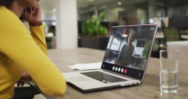 Biracial woman using laptop for video call, with business colleague on screen. Business communication technology and remote home working, digital composite video.