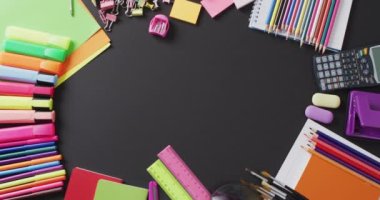 Video of school supplies and notebooks, paper clips, pens over black background. Education, learning and creativity