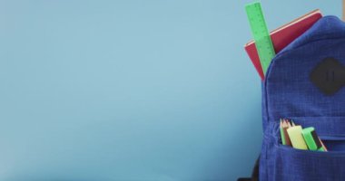 Video of school supplies, notebook, pens, ruler in backpack over blue background. Education, learning and creativity.