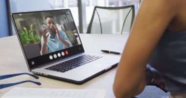 African american woman using laptop for video call, with business colleague on screen. Business communication technology and remote home working, digital composite video.