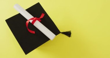 Video of graduation hat lying on yellow background. School equipment, tools, learning and education concept.
