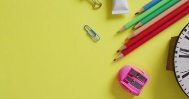 Video of school supplies and notebooks, paper clips, pens over yellow background. Education, learning and creativity