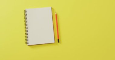 Video of notebook with copy space and pencil on yellow background. School equipment, tools, learning and education concept.