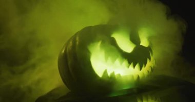 Video of halloween carved pumpkin with smoke and green light on black background. Halloween, autumn, tradition and celebration concept.