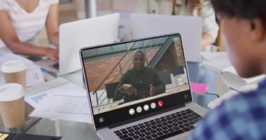 African american woman using laptop for video call, with business colleague on screen. Business communication technology and remote home working, digital composite video.