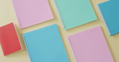 Video of composition with colorful notebooks on yellow surface. School equipment, tools, learning and education concept.