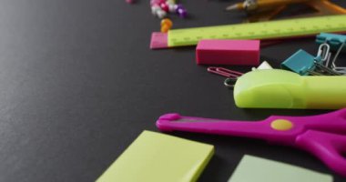 Video of school supplies and notebooks, paper clips, pens over black background. Education, learning and creativity