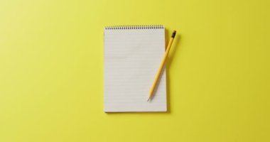 Video of notebook with copy space and pencil on yellow background. School equipment, tools, learning and education concept.