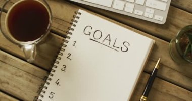 Video of notebook with goals and copy space, coffee and pen on wooden surface. Business, working in office, equipment and tools concept.