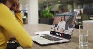 Biracial woman using laptop for video call, with business colleague on screen. Business communication technology and remote home working, digital composite video.